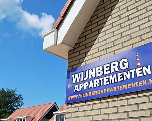 Buitenkant van Wijnberg Appartementen, Hollum, Ameland met logo en blauwe lucht.