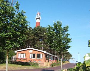Buitenkant van Bij De Vuurtoren appartement met vuurtoren op de achtergrond in Hollum, Ameland.