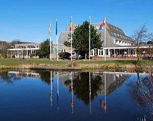 Buitenzijde van Appartementen STRANDHUYS en DE VUURTOREN, Hollum, Ameland, weerspiegeld in rustige vijver.