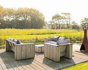 Zonnig terras van De Dijkwachter **** in Ballum, Ameland met houten tuinmeubelen en uitzicht op de natuur.