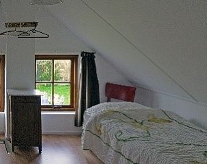 Slaapkamer in vakantiehuis Suzan, Ballum, Ameland met een schuine wand en uitzicht op de tuin, ideaal voor ontspanning.