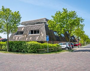 Zijaanzicht van Waddenresidentie Ameland vakantieverblijf in Buren, Ameland, omgeven door groen en parkeerplaatsen.