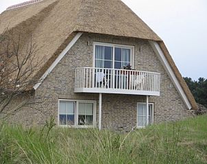 Whirlwind bungalow in Nes, Ameland with thatched roof and private balcony, surrounded by green dunes of the Wadden Islands.