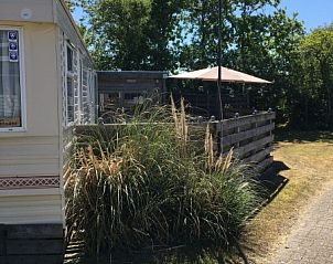 Buitenkant van stacaravan De Hout in Buren, Ameland met groene omgeving.