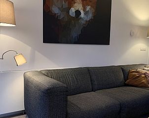 Gezellige zithoek in bungalow Duyngolf 12, Hollum, Ameland met moderne kunst en comfortabele bank, ideaal voor ontspannen vakantie op de Waddeneilanden.