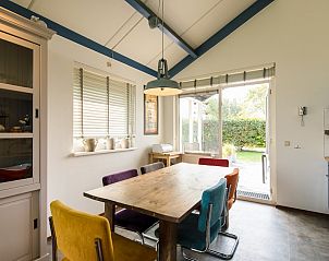 Gezellige eetkamer in Duinvilla 6, een vakantiehuis in Hollum, Ameland, met kleurrijke stoelen en uitzicht op de groene tuin.