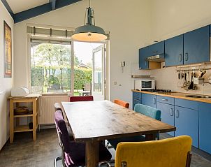 Gezellige keuken in Duinvilla 6, een bungalow in Hollum, Ameland, met kleurrijke stoelen en uitzicht op de tuin van de Waddeneilanden.