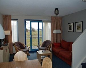 Gemtliches Wohnzimmer in Amelander Kaap Nr. 54, einer Wohnung in Hollum, Ameland mit komfortabler Sitzecke und Blick auf die grne Umgebung.