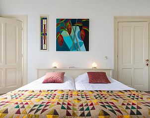 Kunstzinnige slaapkamer in B&B De Postoari Terschelling, Hoorn, met kleurrijke dekens en schilderijen.