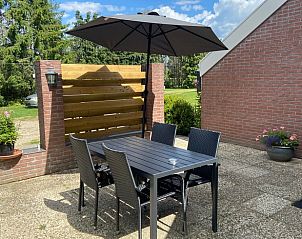 Zonnig terras bij Vakantiehuisje in Odoorn, Midden Drenthe, met tafel, stoelen en parasol voor buitenplezier.