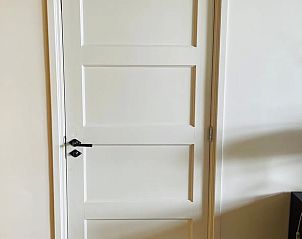 Strakke witte deur in Huisje in Gees, Drenthe, leidt naar sfeervolle binnenruimtes.