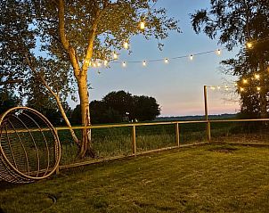 Ontspan in de tuin van Vakantiehuisje in Odoornerveen, Drenthe, met hangstoel en sfeerverlichting bij zonsondergang.