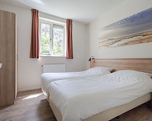 Sfeervolle slaapkamer in Bungalow Zon, vakantiehuis in Dwingeloo, Drenthe, met uitzicht op de groene natuur door een groot raam.