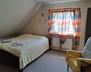Zolder slaapkamer in Vakantiehuis in Boijl, Friesland met comfortabel bed en stoel.