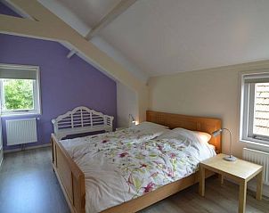 Gezellige slaapkamer in Huisje in Boijl, vakantieaccommodatie in Friese bossen, Friesland, met houten bed en kleurrijke muur.