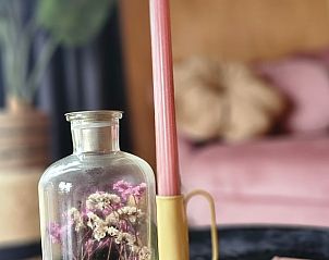Detail van interieur in vakantiehuisje in Westergeest met kaars en bloemen op tafel.