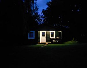 Vakantiehuisje in Munnekeburen verlicht in de avond, omringd door natuur.
