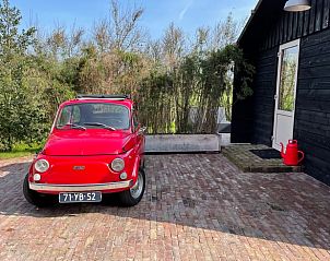 Klassieke rode auto geparkeerd bij vakantiehuis Huisje in Gonga op het Friese platteland.