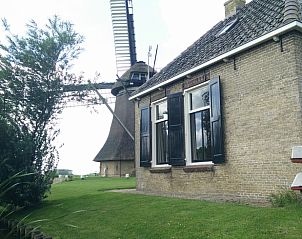 Charmant bakstenen huis bij Vakantiehuis in Achlum, Friesland, met uitzicht op een molen en groene omgeving.