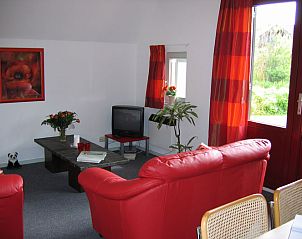 Gezellige woonkamer in Het Kleine Huis, een vakantiehuis in Lauwersmeer, Friesland, met rode accenten en uitzicht op de tuin.
