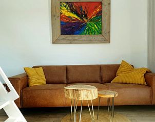 Stijlvolle bank in Vakantiehuisje in Jelsum, Friesland met kleurrijk schilderij en houten tafeltjes.