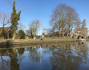 Rustieke charme van Vakantiehuisje in Stiens aan het water, omgeven door bomen op het Friese platteland in Friesland.