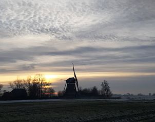 Sfeervolle zonsondergang bij vakantiehuisje in Wyns met silhouet van een molen, Friesland.