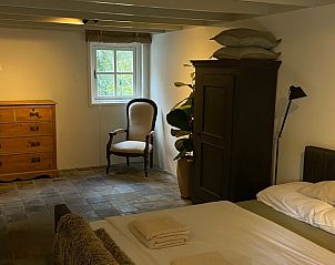 Stijlvolle slaapkamer in Vakantiehuisje in Neerijnen, Rivierengebied met antieke kast en comfortabele stoel.