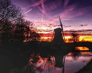 Betoverende zonsondergang bij Huisje in Geldermalsen, vakantiehuis in Gelderland. Prachtig uitzicht op een molen en water in het Rivierengebied.