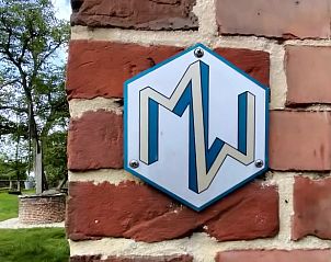 Exterior wall of Cottage in Winterswijk, vacation home in Achterhoek, Gelderland, with rustic sign and green surroundings.