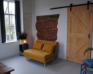 Stijlvolle binnenruimte met bank en houten schuifdeur in Vakantiehuis in Winterswijk Woold, gelegen in de Achterhoek, Gelderland.