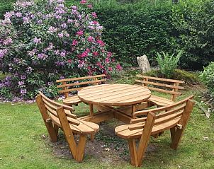 Rond houten zitje in de tuin van Vakantiehuisje in Emst, Veluwe, omringd door bloemen.