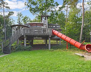 Buitenzijde van Miggelenberg boomhut met glijbaan, omgeven door Veluwse bossen.