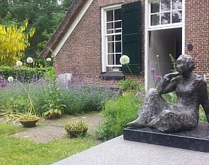 Beeldhouwwerk in de tuin van Huisje in Heerde, Veluwe, omgeven door kleurrijke bloemen in Gelderland.
