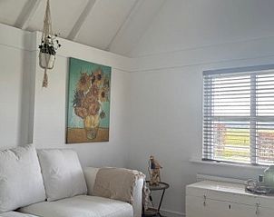 Stijlvolle woonkamer in Huisje in Klarenbeek, Veluwe, met kunst aan de muur en uitzicht op groene velden.