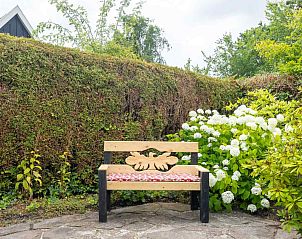 Rustikale Bank im Garten des Ferienhauses GR032, Lauwersoog, umgeben von Blumen.
