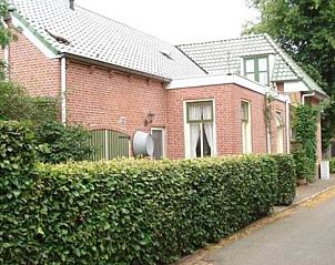 Bakstenen gevel van Vakantiehuis in Vriescheloo omgeven door groene heg in Groningen.