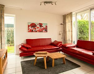 Gezellige woonkamer van Standaard 6 bungalow in Vlagtwedde, Zuidoost Groningen, met rode banken en uitzicht op de groene tuin.