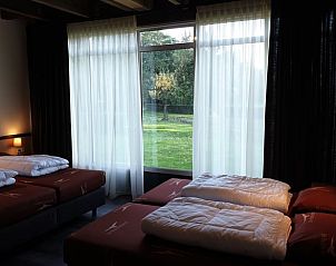 Ruime slaapkamer met grote ramen in Vakantiehuis in Schaijk, omgeven door groene natuur in Noordoost Brabant.