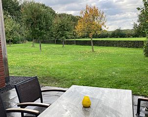 Buitenterras met uitzicht op groene tuin in Vakantiehuis in Schaijk, Noordoost Brabant, ideaal voor buitenmaaltijden.