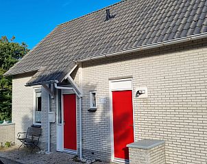 Front view of vacation home NH549 in Callantsoog, North Sea coast, North Holland, with red doors and green surroundings.