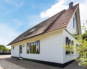 Detached house in Callantsoog, North Sea coast, North Holland, vacation home with thatched roof and attractive facade under blue sky.