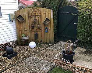 Charmante tuinpoort bij chalet Laat je ziel bungelen in Onderdijk, met decoratieve elementen en groene omgeving.