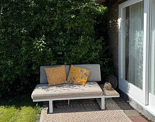 Gezellige zithoek op het terras van Vakantiehuisje in Schoorl, Noord-Holland omringd door groen.