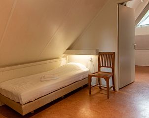 Eenvoudige slaapkamer in Vakantiehuis 6-persoons, Dalfsen, met houten stoel en bedlampje.