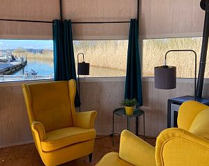 Gezellige binnenruimte van Huisje in IJsselstein, vakantiehuis gelegen in Utrecht, met comfortabele gele fauteuils en uitzicht op het water.