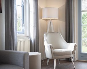 Gemtliche Sitzecke im Bungalow T6 Comfort, Domburg, Walcheren, mit bequemem Sessel und Blick auf den Garten durch groe Fenster.