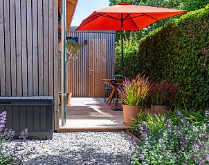 Geniet van de zonnige veranda bij Vakantiehuis in Biggekerke, Walcheren, Zeeland, met kleurrijke parasol en groene omgeving.