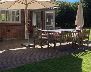 Terras van Vakantiehuisje in Goedereede met houten meubels en parasol op Goeree-Overflakkee.