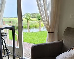 Uitzicht vanuit de woonkamer van Huisje in Haastrecht, vakantieaccommodatie in Zuid-Holland, op groene velden.